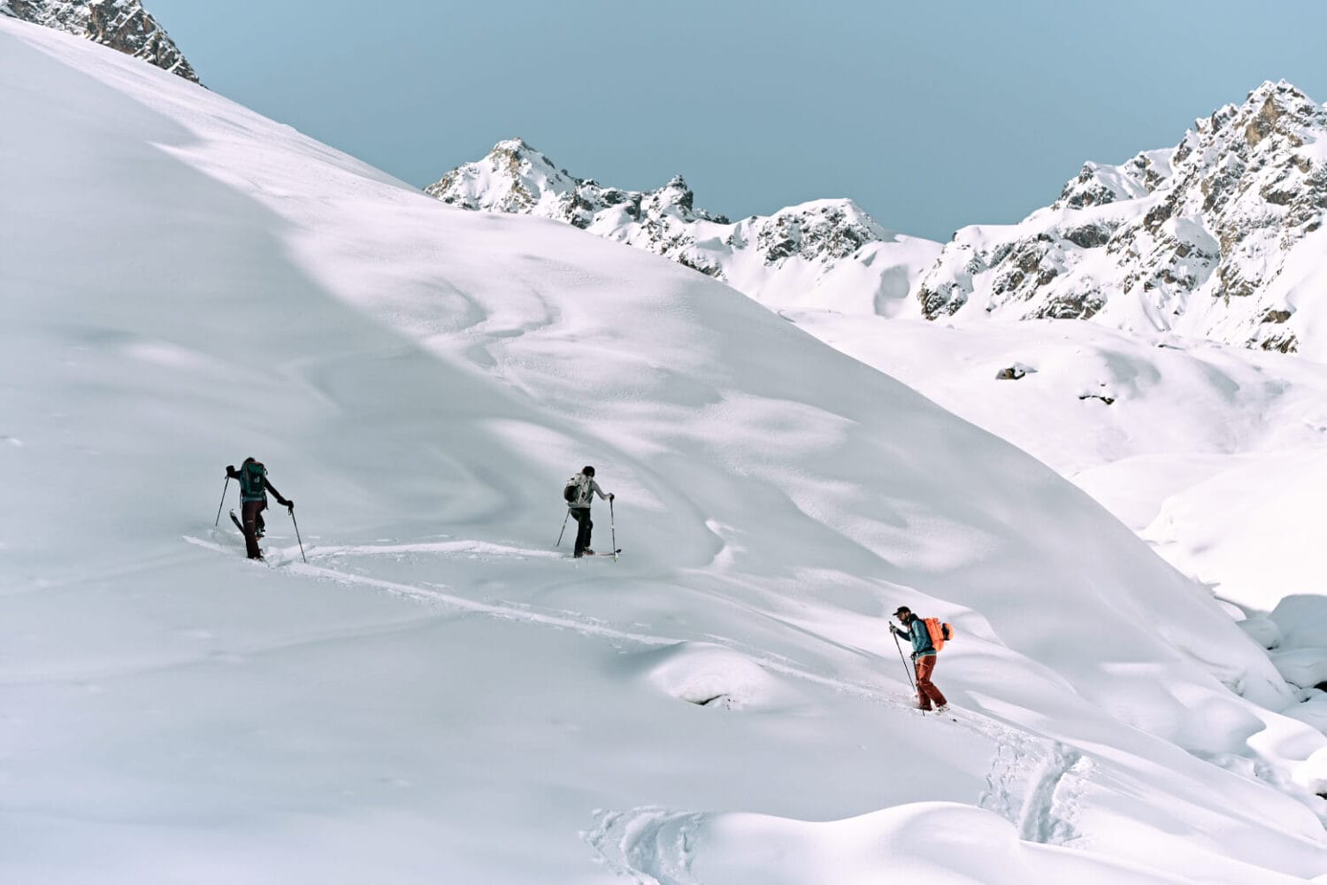 Eine Gruppe Skifahrer wandern im Schnee auf einen Berg, im Hintergrund Bergpanorama.